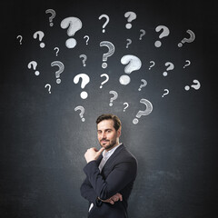 Thoughtful businessman standing in front of dark background with floating question marks symbolizing curiosity, problem-solving, and decision-making.