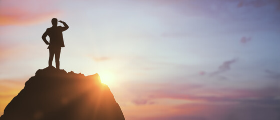 Silhouette of businessman standing on mountain peak looking toward sunrise on colorful sky background, symbolizing vision and leadership success. © Who is Danny