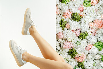 Beautiful female legs in sneakers. Place for text. shoe advertising. Girl in sneakers against the background of flowers