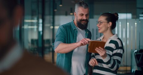 Male senior coach or speaker sharing business ideas and collaborating with a diverse team in a modern office, presenting a project on a tablet during a brainstorming session in a startup hallway - Powered by Adobe