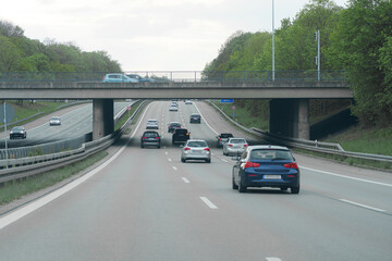 Cars traveling on a highway under a bridge surrounded by trees on a cloudy day