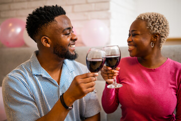 Happy young couple celebrating woman's birthday at home. They are toasting with wine.