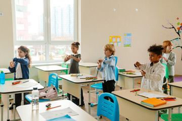 Obraz premium A concentrated curly Black school-aged boy and other serious multi-ethnic schoolchildren are standing at their desks doing exercises in the classroom.