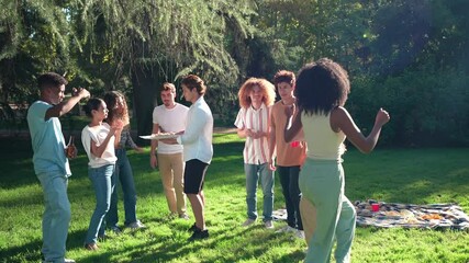 Diverse group of young friends dancing, sharing laughter and enjoying summer picnic moments on green grass with vibrant energy and carefree spirit