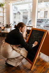 Side view of a serious dark-haired European female owner in her early 30s in a black sweater and...