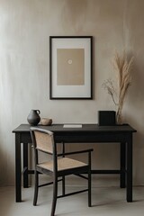 Minimalist workspace with a neutral color palette. A black wooden desk, chair with cane back, and a framed print on a beige wall. Dried pampas grass in a vase on the desk adds a touch of texture