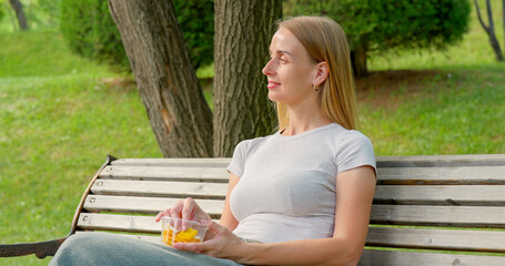 Woman relaxing on a bench in the park while eating dried mango slices