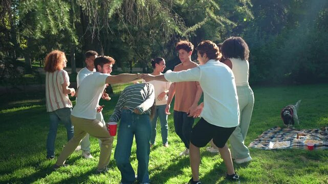 Group of cheerful young friends playing red rover game, running and laughing together on sunny grass covered park area during summer weekend leisure time