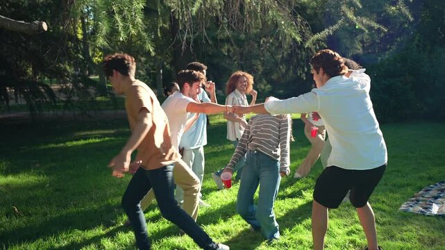 Group of diverse friends enjoying a picnic in a park, playing limbo and having fun in slow motion