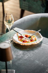 A stylish dining scene featuring a plate of colorful salmon dish alongside a glass of sparkling wine. The elegant setting enhances the gourmet experience.