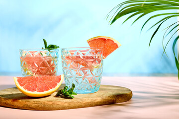 Refreshing chilled drinks with grapefruit and fresh mint in the bright rays of the sun under palm leaves. Summer refreshing cocktails