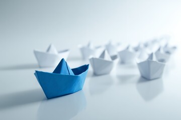A single blue paper boat leads a fleet of white ones on a reflective surface, concept for business leadership and innovation