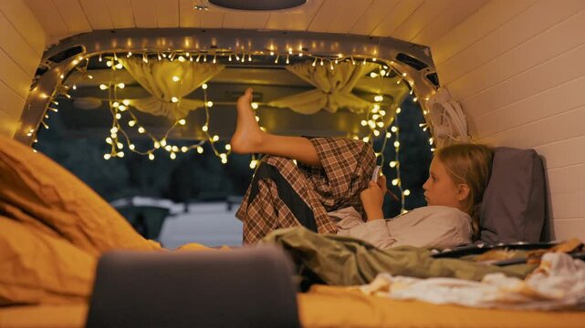 10 year old girl enjoys a peaceful night in her van, using her phone surrounded by warm lighting and comfortable bedding