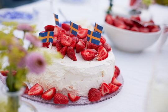 A close up of a table set with a cake of strawberries and whipped cream and a bowl of straberries in the background