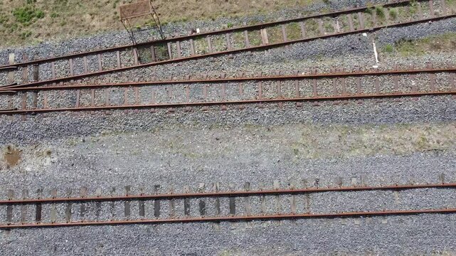 Camera looking down and moving sideways along two rows of rusted railway tracks.