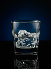 Vodka with ice on a black reflective background.