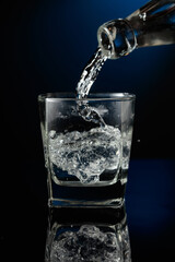 Crystal clear vodka being poured over ice in a glass.