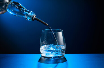 Vodka pours from bottle to glass with ice.