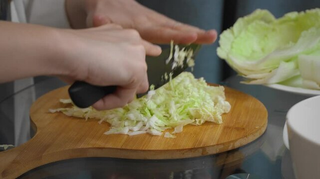 Professional female chef carefully slices fresh Chinese nappa cabbage on a wooden cutting board, prepares clean, bright ingredients for a nutritious meal in a modern kitchen setting