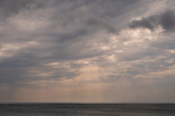 Sun between dark storm clouds over ocean. Dramatic seascape. Clouds and rain flurry over sea.