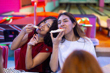 Two young women eating pizza at bowling alley restaurant