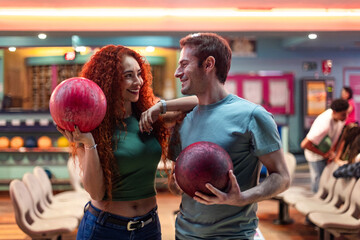 Happy couple holding bowling balls and smiling at bowling alley