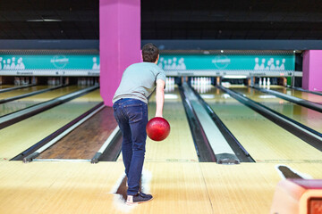 Young man throwing bowling ball in modern bowling alley