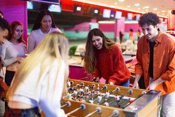 Friends playing foosball table in bowling alley having fun