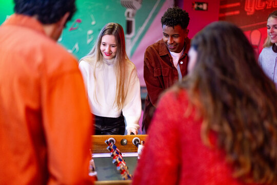 Friends playing foosball table soccer game in arcade