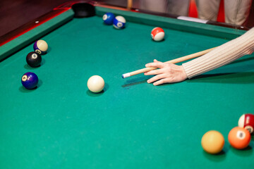 Woman playing billiards aiming white ball on green table
