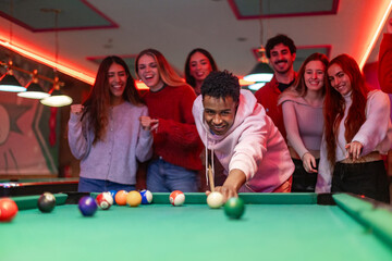 Young man playing billiard with friends cheering him up in a pub