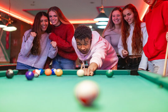 Young man playing pool with friends cheering in a pub