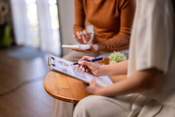 Two women are sitting at a table with a clipboard and pens