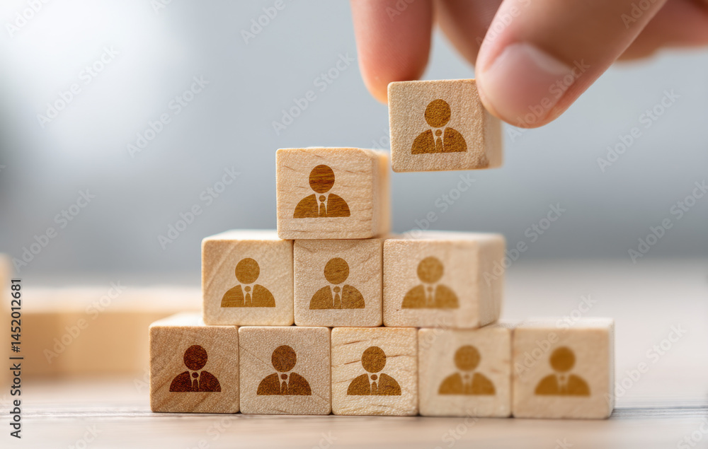 Poster a hand arranges wooden blocks with human icons, forming a pyramid. this setup symbolizes collaborati
