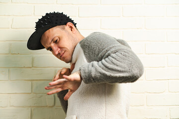 A man wearing a black cap and a gray sweater is captured in motion, dancing gracefully with fluid movements. His outfit contrasts against the background as he enjoys his dance.