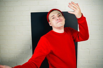 A man in a red hoodie and hat dances against a white brick wall