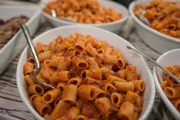 Detail of a restaurant buffet banquet with several trays of large portions of tomato pasta served for lunch