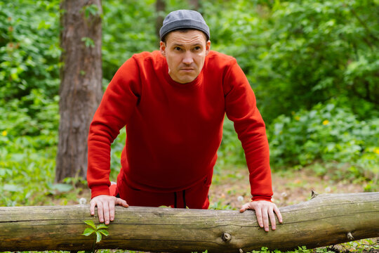 A man performs push-ups using the log as support. The backdrop is a dense forest with trees and foliage.