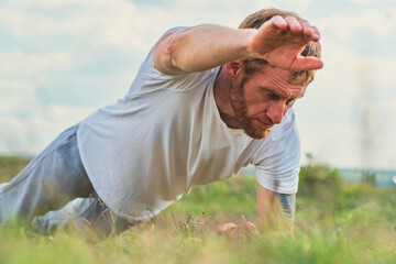 A focused man performs push-ups on a grassy field during early morning hours