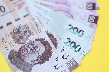 Mexican pesos money bills in big amount lies on yellow color table close up