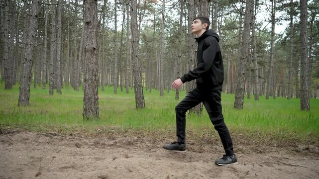 Teenager walks quickly through dense pine forest. Adolescent boy hurries through thick pine woods. Young male briskly walks across dense forest with pine trees