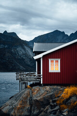 Charming Red Cabin Nestled by the Tranquil Waterside with a Stunning Mountain Backdrop