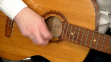 Hand strumming classic acoustic guitar during casual music session indoors. Fingers plucking strings of traditional six string instrument in relaxed indoor setting. Hands playing melodies on wooden