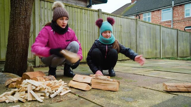 Mother and daughter handling firewood, tossing logs and arranging kindling. Exciting family moments Living moments together. Woman and girl crouching near wooden pile, sorting pieces and playfully