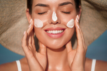 Beautiful woman applying cream sunscreen on tanned face. Sunscreen concept. Skin and body care. The...