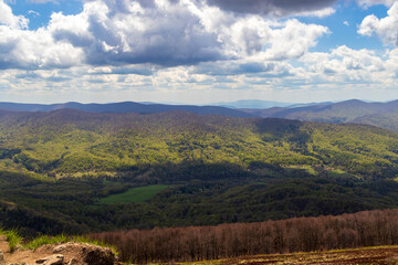 Panoramic view of the lush green Bieszczady Mountains under a partly cloudy sky, showcasing vibrant...