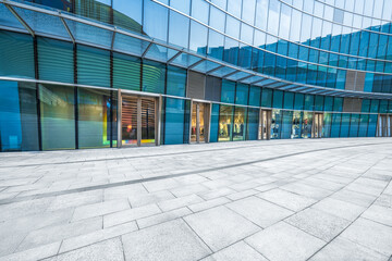 Empty brick floor outside a modern building exterior featuring a large blue glass curtain wall...