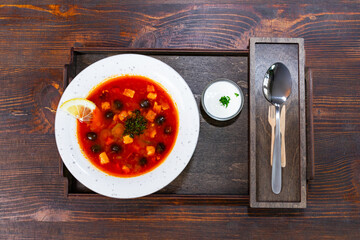 Delicious red borsch served with cream and lemon on wooden tray
