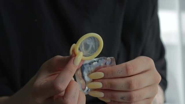 A girl unpacks a package with a condom.
A packaged condom in a shiny package in a woman's hands.
Safe sex
