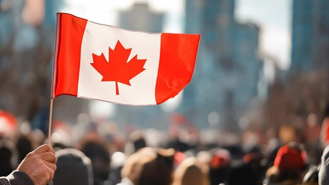 Hand holding Canadian flag at outdoor public event in daytime. Patriotism and national celebration concept. Canada day scenic with red maple leaf and city background.